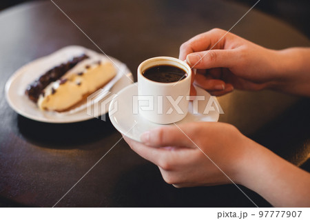 close up mug of coffee in the hands and a sweet dessert on a plate 97777907