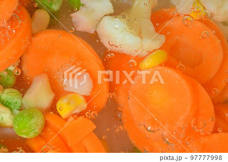 Close-up fresh soup vegetables with carrots, peas, cauliflower and corn on white background. Soup vegetables with carrots, peas, cauliflower and corn in boiling water on white background, close-up 97777998