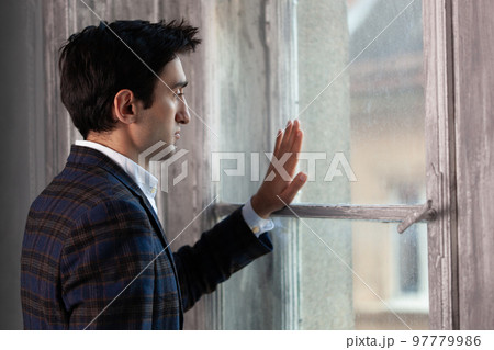 a handsome man is sad near the window touching with his hand. 97779986