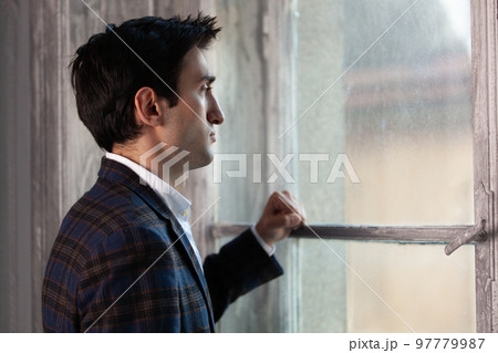 a handsome man is sad near the window touching with his hand. 97779987