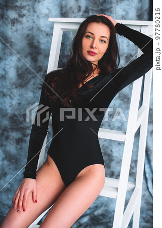 Smiling attractive young woman with sexy shapely forms, loose wavy hair, red lipstick and slim body is posing in the black body, studio retouched photoshoot, blue background. Grain texture is added Smiling attractive young woman with sexy shapely forms, loose wavy hair, red lipstick and slim body is posing in the black body, studio retouched photoshoot, blue background. Grain texture is added 97780216