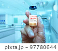 A close-up hand with a glove holding COVID-19 vaccine over a blurred hospital background 97780644