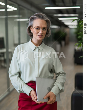 Mature caucasian woman stands with a laptop among the office.  97780900