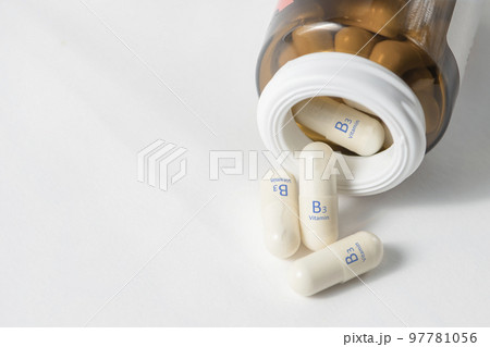 Vitamin B3. Vitamins in capsules. White capsules with vitamin B3, niacinamide or nicotinic acid are scattered on the table from a bottle on a white background. Dietary supplements in tablets. 97781056