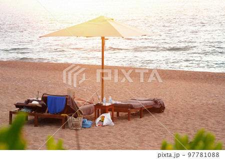 Woman resting comfortably on sunbeds under white sun umbrella. Perfect vacation concept. Soft yellow sunlight. Candid photo. 97781088