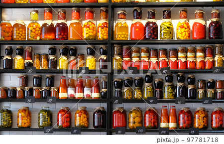 Variety glass jars of homemade pickled or fermented colorful vegetables and jams on the shelves in the food market. Fermented food concept. Variety glass jars of homemade pickled or fermented colorful vegetables and jams on the shelves in the food market. Fermented food concept. 97781718