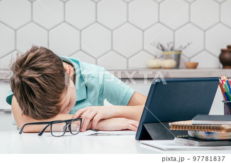 Portrait of young preteen weary pupil lying sleeping on hand on desk near notebooks, glasses, color pencils, tablet. Portrait of young preteen weary pupil lying sleeping on hand on desk near notebooks, glasses, color pencils, tablet. 97781837