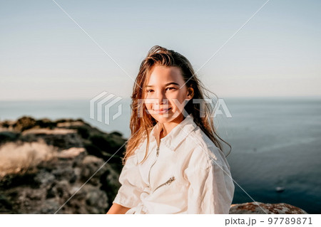 Adorable teenage girl outdoors enjoying sunset at beach on summer day. Close up portrait of smiling young romantic teenager girl with long hair on beach at summer evening. Travel and holidays Adorable teenage girl outdoors enjoying sunset at beach on summer day. Close up portrait of smiling young romantic teenager girl with long hair on beach at summer evening. Travel and holidays 97789871