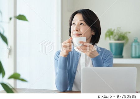 パソコン作業の合間にコーヒーを飲むミドル女性 97790888
