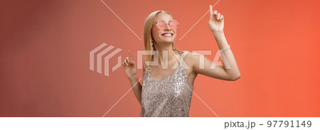 Delighted carefree attractive stylish millennial blond woman celebrating partying having fun wear sunglasses trendy silver dress dancing closed eyes broad smile waving hands up, red background Delighted carefree attractive stylish millennial blond woman celebrating partying having fun wear sunglasses trendy silver dress dancing closed eyes broad smile waving hands up, red background 97791149