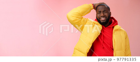 Upset gloomy african-american bearded guy in yellow jacket red hoodie hold hands cringing regret face disaster terrible situation expressing sorrow crying sobbing, standing pink background 97791335