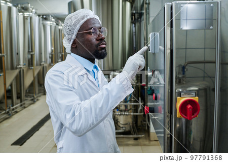 African American engineer in uniform working on machinery, he pushing button on equipment during his work at brewery 97791368