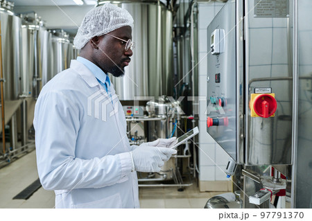 African American engineer in uniform controlling the equipment with tablet pc standing in front of equipment in workshop African American engineer in uniform controlling the equipment with tablet pc standing in front of equipment in workshop 97791370