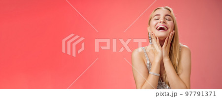 Waist-up joyful accomplished charming rich blond woman in silver stylish evening dress touching cheeks happily smiling laughign carefree close eyes tender have fun relaxing party dance floor 97791371