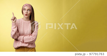 Lightbulb, I have idea. Amused and enthusiastic creative young female project manager raising index finger, showing eureka gesture folding lips intrigued looking up suggesting plan came to mind 97791763