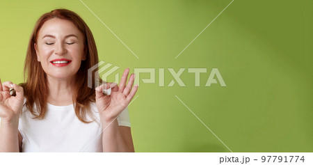 Close to perfection. Close-up peaceful relaxed redhead happy woman closed eyes pure delighted smile show zen peace satisfaction gesture meditating reach nirvana calm stand green background Close to perfection. Close-up peaceful relaxed redhead happy woman closed eyes pure delighted smile show zen peace satisfaction gesture meditating reach nirvana calm stand green background 97791774