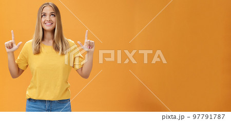 Portrait of upbeat joyful beautiful young caucasian girl with tan and fair hair looking and pointing up, smiling cheerfully watching fireworks posing amused and happy against orange background Portrait of upbeat joyful beautiful young caucasian girl with tan and fair hair looking and pointing up, smiling cheerfully watching fireworks posing amused and happy against orange background 97791787