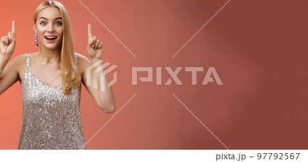 Charming amazed blond european woman in fabulous silver glittering dress raise hands point up amused enjoying watching shooting stars, fireworks gaze camera excited happy surprised, red background Charming amazed blond european woman in fabulous silver glittering dress raise hands point up amused enjoying watching shooting stars, fireworks gaze camera excited happy surprised, red background 97792567