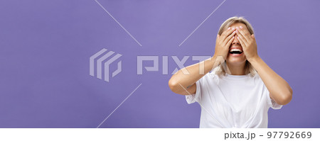Can I look now. Portrait of excited pleased attractive tanned girlfriend in white t-shirt closing eyes and smiling broadly waiting for boyfriend bring surprising gift over purple background 97792669