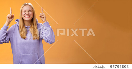 Hopeful charming blond female student praying win first prize achieve dream lifetime hope fortune her side close eyes smiling thrilled pointing up anticipating good news standing orange background Hopeful charming blond female student praying win first prize achieve dream lifetime hope fortune her side close eyes smiling thrilled pointing up anticipating good news standing orange background 97792808