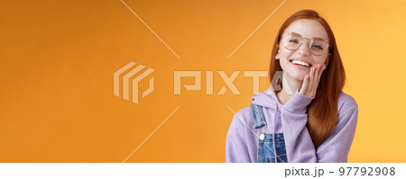 Charismatic happy tender redhead smiling european girl 20s glasses hoodie denim overalls having fun enjoying summer holidays chilly evening laughing joyfully touch pure clear skin, orange background Charismatic happy tender redhead smiling european girl 20s glasses hoodie denim overalls having fun enjoying summer holidays chilly evening laughing joyfully touch pure clear skin, orange background 97792908