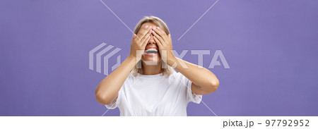 Can I look now. Portrait of excited pleased attractive tanned girlfriend in white t-shirt closing eyes and smiling broadly waiting for boyfriend bring surprising gift over purple background Can I look now. Portrait of excited pleased attractive tanned girlfriend in white t-shirt closing eyes and smiling broadly waiting for boyfriend bring surprising gift over purple background 97792952