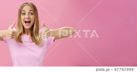Supportive girlfriend cheering for favorite player showing thumbs up with happy positive smile giving approval and showing she likes perfect idea posing amused and enthusiastic against pink background Supportive girlfriend cheering for favorite player showing thumbs up with happy positive smile giving approval and showing she likes perfect idea posing amused and enthusiastic against pink background 97792999