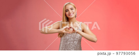 Romantic passionate charming lovely blond glamour woman in silver dress brilliants show heart love gesture express sympathy passion, adore relationship smiling delighted, standing red background 97793056