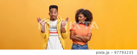 Jeez man what your problem. Offended displeased african american stylish and attractive girlfriend looking at boyfriend acting cool pretending he uninvolved shrugging with sorry look and smiling 97793235