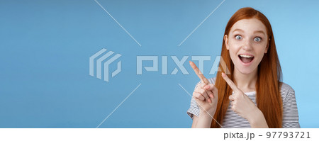 Charismatic impressed surprised good-looking happy smiling cute redhead girl say wow grinning astonished wide eyes pointing upper left corner stunned thrilled speechless see awesome promo 97793721