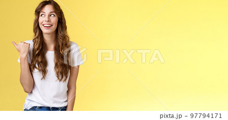 Something interesting right there. Curious lively enthusiastic charming woman glancing pointing thumb left smiling broadly discuss cool event laughing carefree stand yellow background 97794171