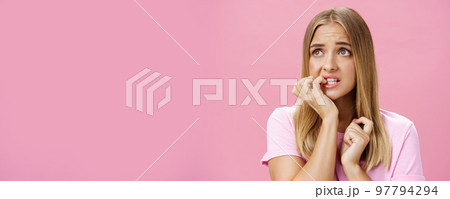 Girlfriend broke car feeling cocnerned and scared of man walking towards to argue looking aside with anxiety and panic biting fingernails from stress and troublesome situation posing over pink wall 97794294