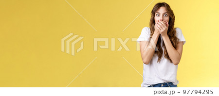 Shocked ambushed speechless cute girl hear impressive rumor shut mouth hold hands lips stare camera astonished eavesdrop juicy stunning conversation stand yellow background 97794295