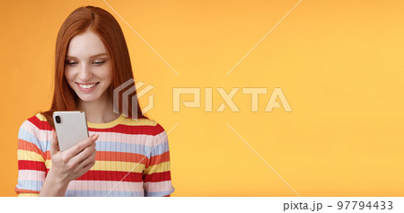 Charming modern redhead girl college student checking message box holding smartphone look happy smiling delighted cellphone display receive hundred likes photo post online, orange background Charming modern redhead girl college student checking message box holding smartphone look happy smiling delighted cellphone display receive hundred likes photo post online, orange background 97794433