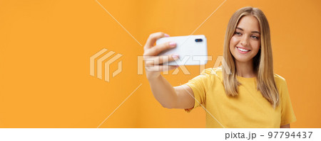 Waist-up shto of outgoing and charismatic pretty confident woman with no makeup and tanned skin holding smartphone pulled on distance smiling broadly at cellphone screen while taking selfie 97794437