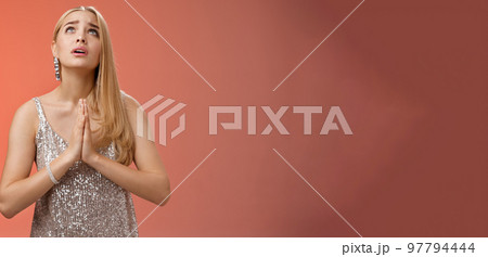 Hopeful worried concerned faithful blond woman in silver dress praying talking god wishing family okay press palms together supplicating nervously begging, standing red background stylish dress 97794444