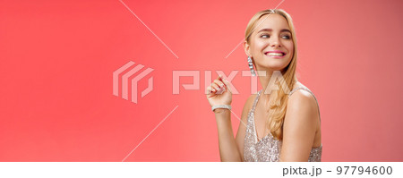Elegant glamour gorgeous young rich blond woman attend charity party in stylish silver glittering dress accessorize turning right smiling greeting familiar person grinning joyfully, red background 97794600