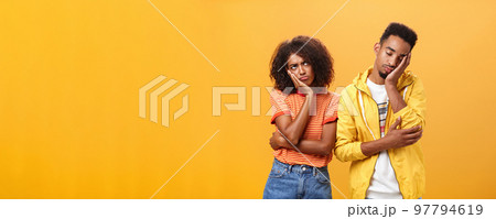 Girl feeling displeased and offended on boyfriend who fell asleep during date pursing lips frowning looking up while boyfriend leaning head on face with closed eyes and tired look over orange wall Girl feeling displeased and offended on boyfriend who fell asleep during date pursing lips frowning looking up while boyfriend leaning head on face with closed eyes and tired look over orange wall 97794619