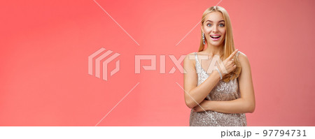 Joyful surprised good-looking blond woman talking friend during party smiling broadly look camera amused wondered pointing upper right corner curious discuss awesome room design, red background 97794731