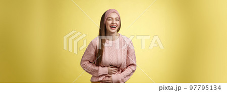 Amused and entertained charming young european female student laughing till belly hurts from giggle smiling holding palms on stomach, having fun enjoying watching funny comedy over yellow wall 97795134