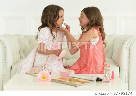 Cute sisters sitting on sofa appying cosmetics Cute sisters sitting on sofa appying cosmetics 97795174