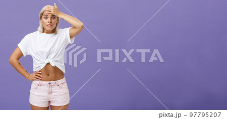 Damn I am in trouble. Worried troubled good-looking stylish female employee with tanned skin and fit body holding hand on forehead popping eyes from anxiety and making nervous face over purple wall 97795207