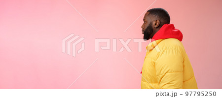 Profile studio shot bearded young 25s african guy in yellow jacket red hoodie look left normal unbothered relaxed expression standing queue order fastfood pink background, waiting take-away 97795250