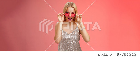 Sassy carefree daring young blond girl winking cheeky smiling assertive making first move approach handsome man nightclub asking dance standing red background touching sunglasses wear dress 97795515