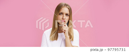 Girl facing problem thinking being hesitant while making decision holding hand on chin frowning pursing lips standing thoughtful over pink background in white casual t-shirt Girl facing problem thinking being hesitant while making decision holding hand on chin frowning pursing lips standing thoughtful over pink background in white casual t-shirt 97795731