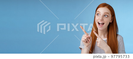 Amused adorable redhead european girl say wow stare gasping astonished pointing looking upper left corner excited smiling drop jaw amazed standing thrilled blue background excitement concept Amused adorable redhead european girl say wow stare gasping astonished pointing looking upper left corner excited smiling drop jaw amazed standing thrilled blue background excitement concept 97795733
