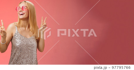 Positive charming european carefree stylish girlfriend having fun dance-floor show victory peace signs look up happily smile in sunglasses glamour glittering dress enjoy celebration, red background Positive charming european carefree stylish girlfriend having fun dance-floor show victory peace signs look up happily smile in sunglasses glamour glittering dress enjoy celebration, red background 97795766