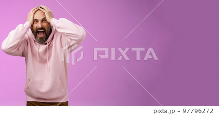 Outraged furious mad adult man bearded yelling shocked despair hatefully looking camera insane holding hands head frowning shouting losing bet disappointed very upset standing purple background 97796272