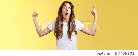 No way omg stunning. Impressed surprised caucasian curly-haired girl long hair drop jaw gasping astonished stare popping eyes look up pointing top copy space interested curiously observe 97796301