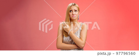 Upset doubtful unsure cute blond funny glamour girl in silver evening dress cringing grimacing hesitant pointing looking upper right corner suspicious, uncertain standing red background Upset doubtful unsure cute blond funny glamour girl in silver evening dress cringing grimacing hesitant pointing looking upper right corner suspicious, uncertain standing red background 97796560